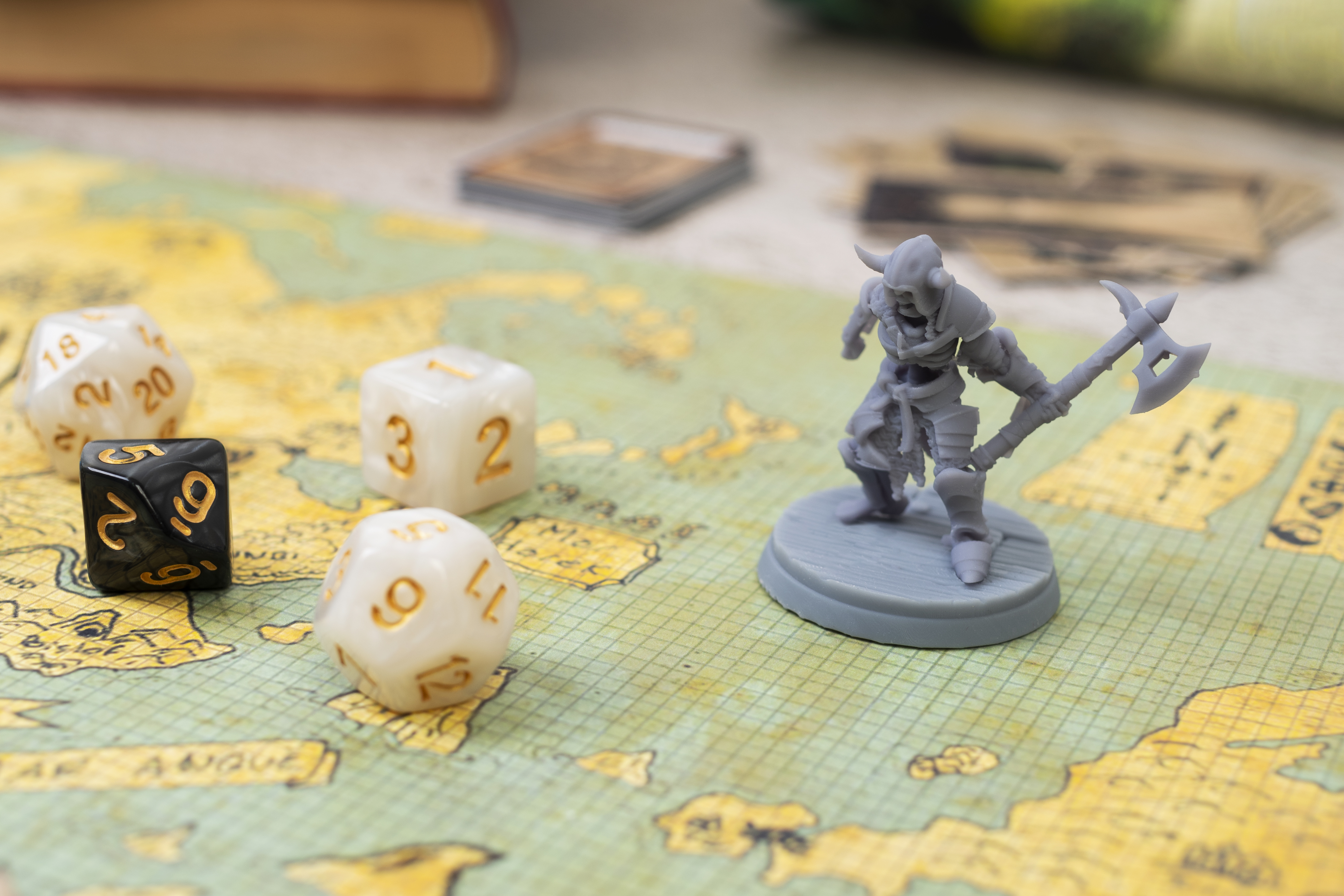 Uma miniatura de personagem cinza, possivelmente de um jogo de tabuleiro, está posicionada sobre um mapa antigo.